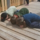 Kinder knien auf dem Boden und schauen durch die Holzdielen.